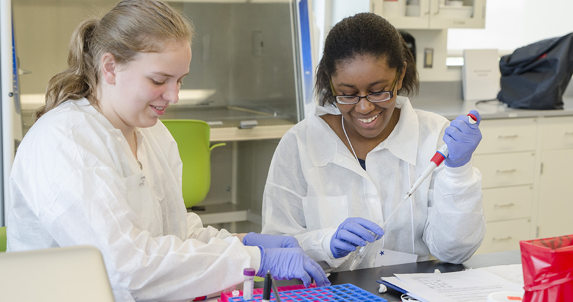 students using a pipette in a lab and smiling