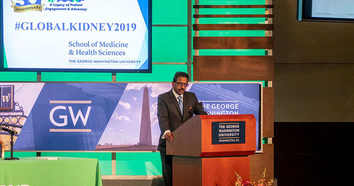 Dr. Dominic Raj speaking from a GW podium on a stage displaying '#GLOBALKIDNEY2019'