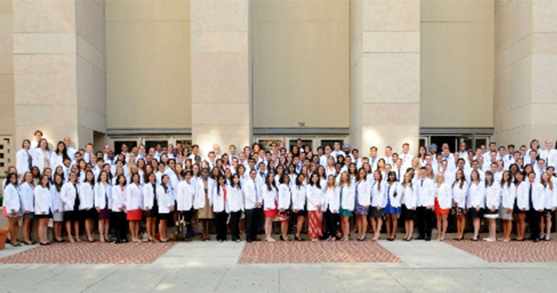 Dozens of MD students in white coats posing together