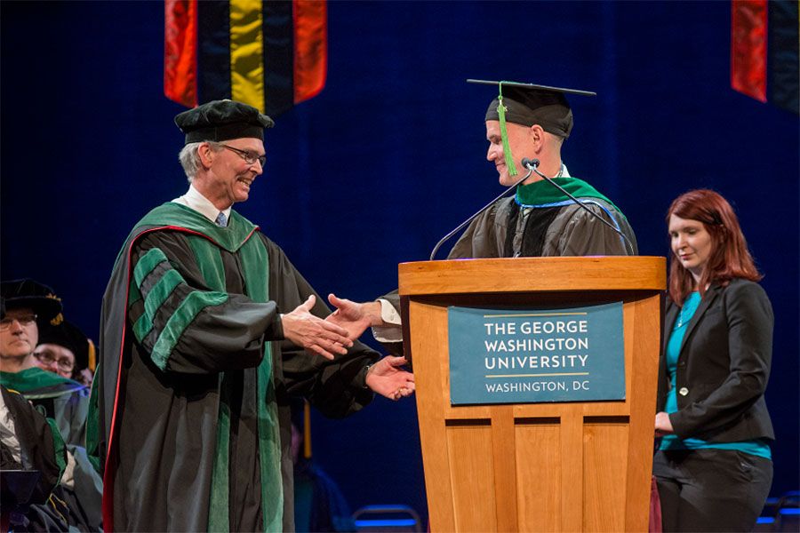 Scott Schroth, M.D., and Ray Lucas, M.D. shaking hands on stage in graduation regalia