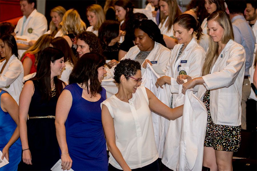 First-year PA students putting on white coats in a room full of people