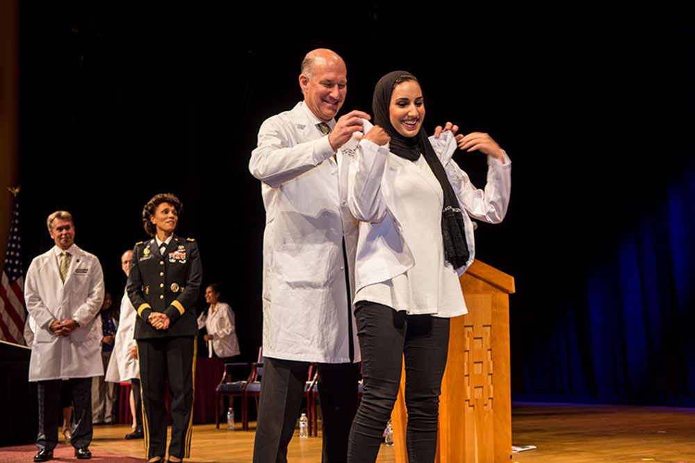 Dean Jeffrey Akman placing a white coat on a medical student
