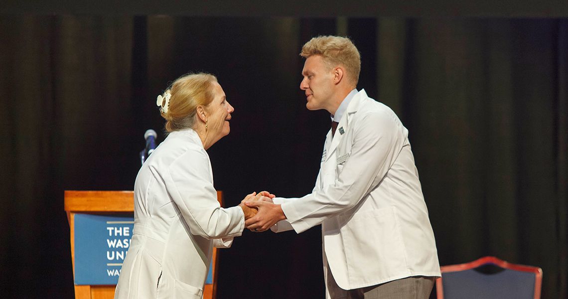 Dean Bass shakes hands with student wearing new white coat