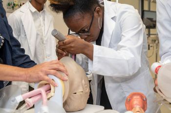 A medical student practices an oral procedure on a mannequin head