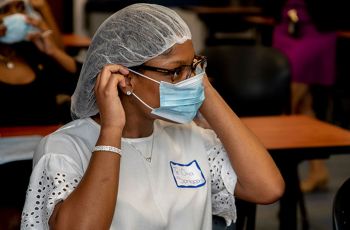 A DC HEAL participant putting on a facemask and hairnet