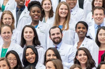 Members of the GW MD program class of 2022 standing together wearing white coats