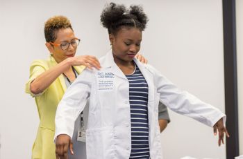 Yolanda Haywood, M.D., helps a DC HAPP participant put on her white coat
