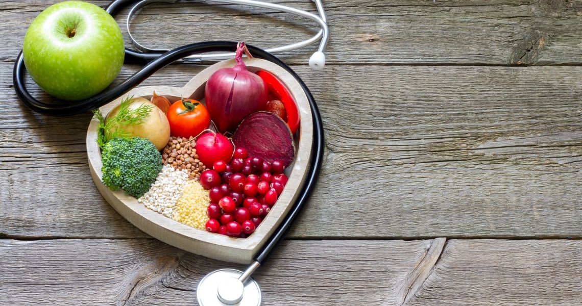 heart shaped box filled with vegetables and surrounded by a stethoscope and an apple