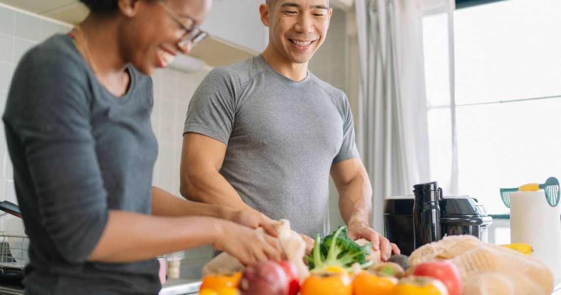 Two people cooking with vegetables in a kitchen and smiling