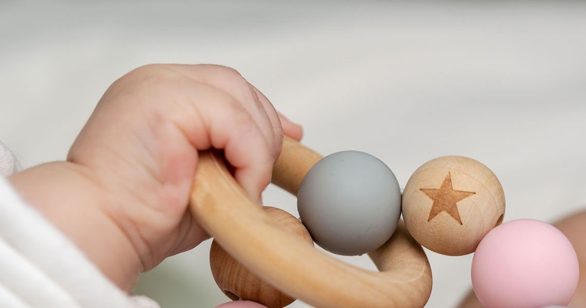 A baby's hand grips a wooden ring and ball chain toy