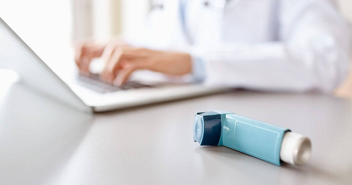 An inhaler sits next to a doctor typing on a laptop 