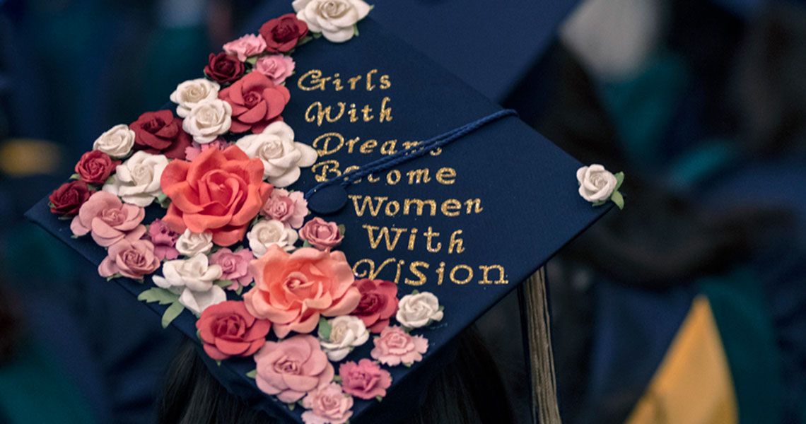 A graduate wearing a cap with pink, white and red flowers and reads 'Girls with dreams become women with vision'