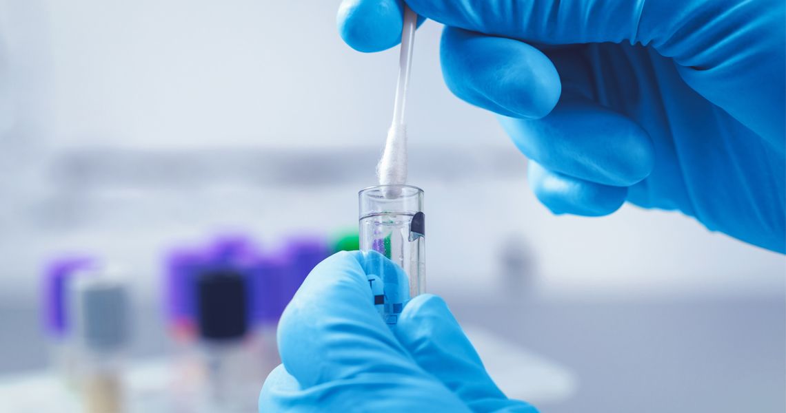 Gloved hands remove a sample swab from a vial in a lab