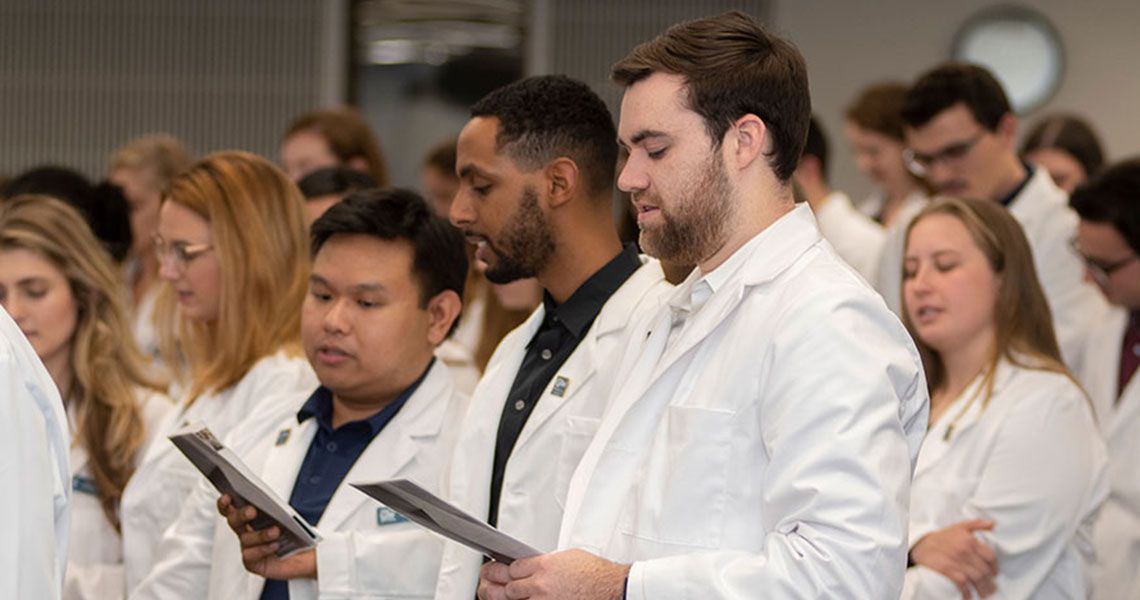 Physician Therapy student wearing white coats recite from a pamphlet