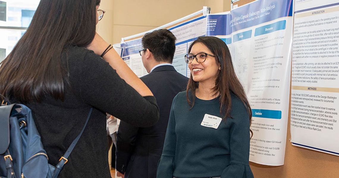 Two medical students speak to each other in front of a presentation poster