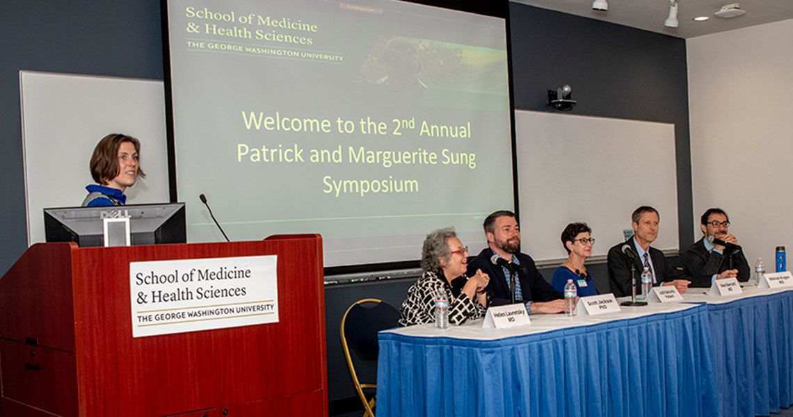 A person standing at a podium and five panelists sitting at a table | Welcome to the 2nd annual Patrick and Marguerite Sung Symposium