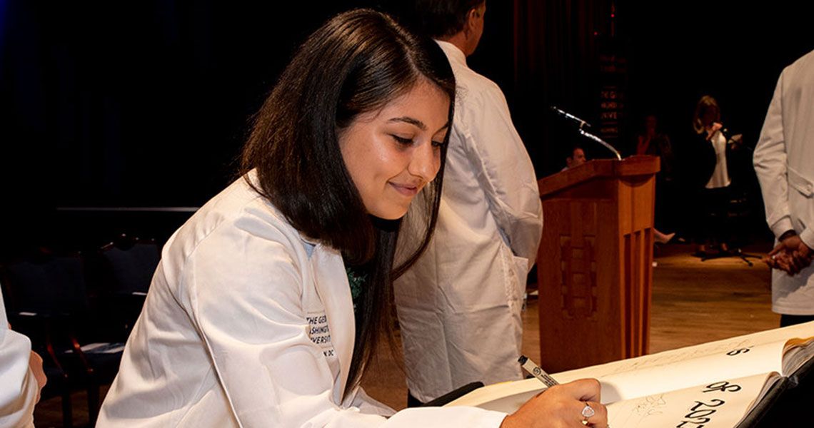 A GW MD student in a white coat signs a ceremonial oath