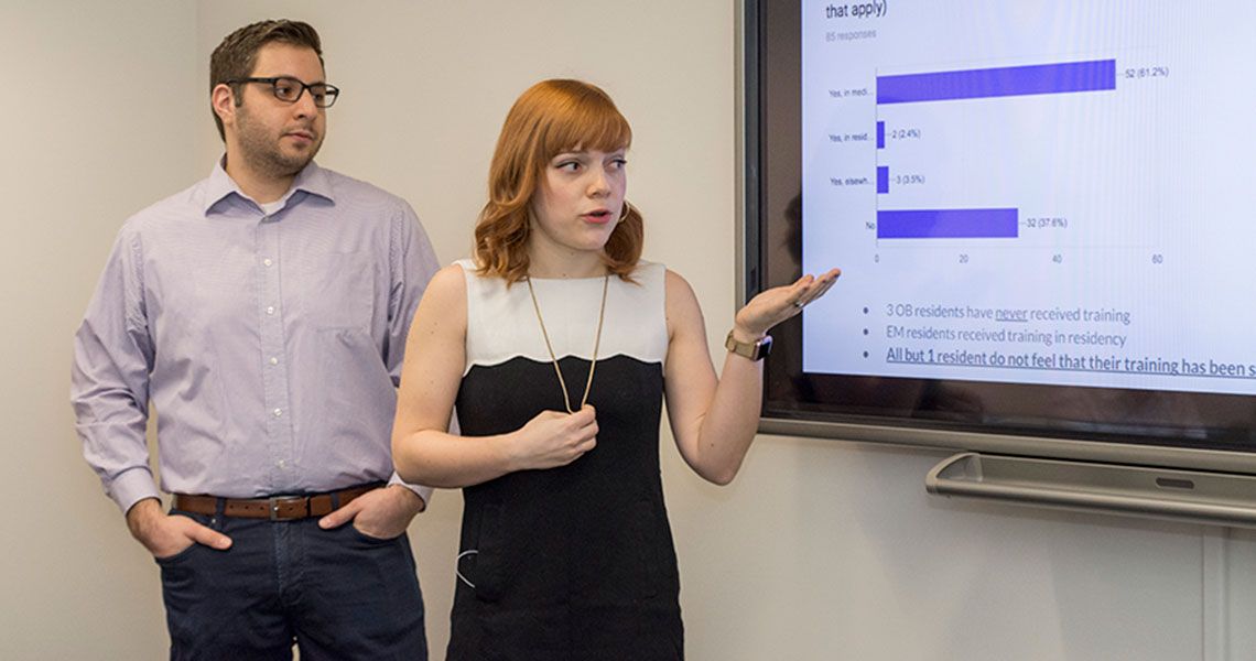 Two GW medical students presenting next to a screen with a bar graph