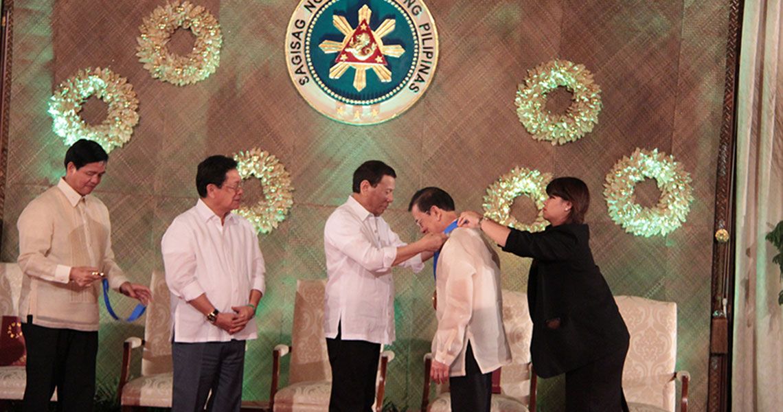 Philippines President Rodrigo Duterte placing a medal on Dr. Pedro A. Jose in a ceremonial room