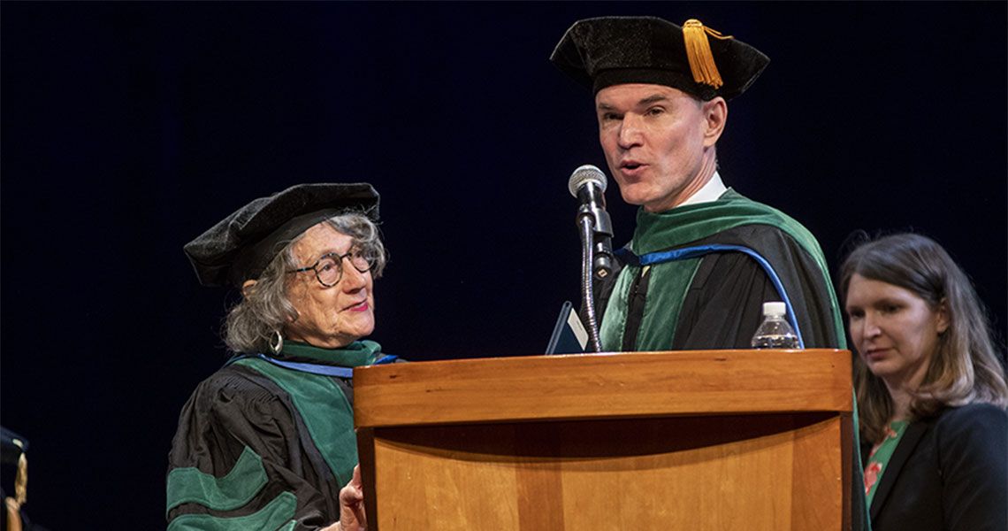 Two GW faculty members wearing ceremonial regalia standing near a podium