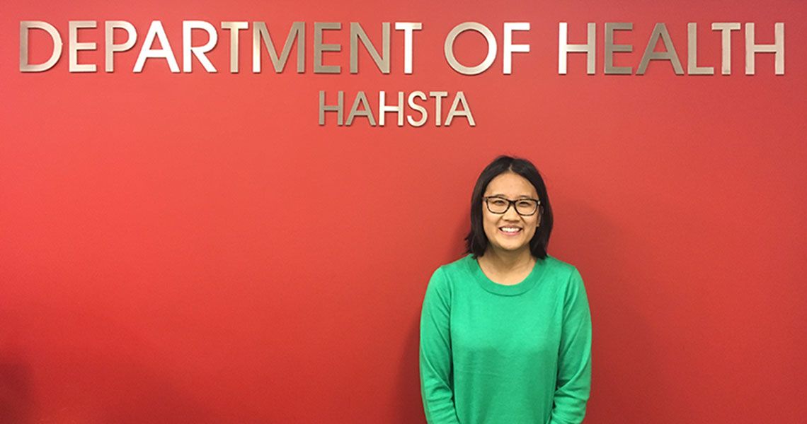 Linda Yang standing in front of a red wall with the sign "Department of Health HAHSTA"