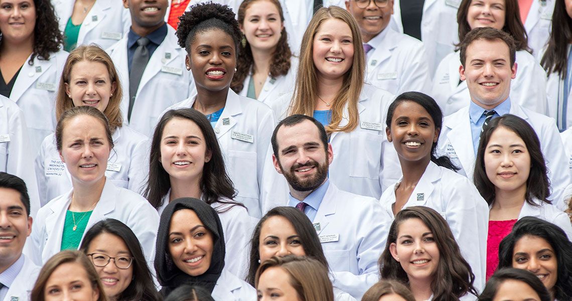 Members of the GW MD program class of 2022 standing together wearing white coats