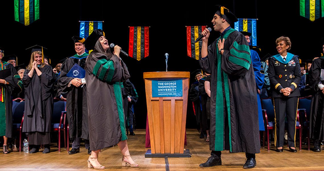 Two GW medical students singing onstage at graduation 