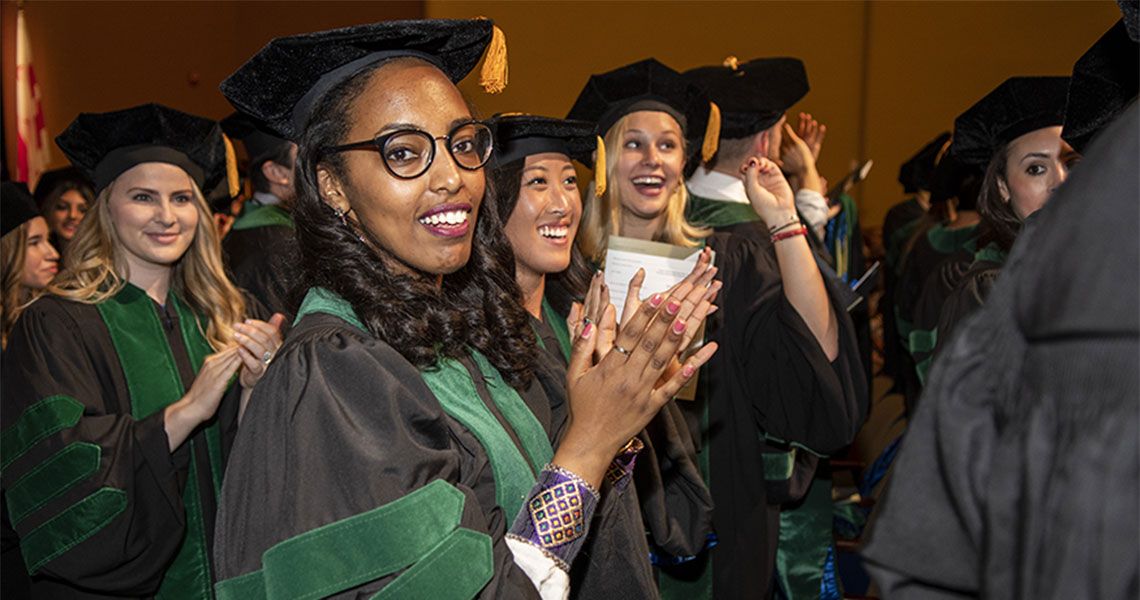 GW MD Program students wearing graduation regalia and clapping