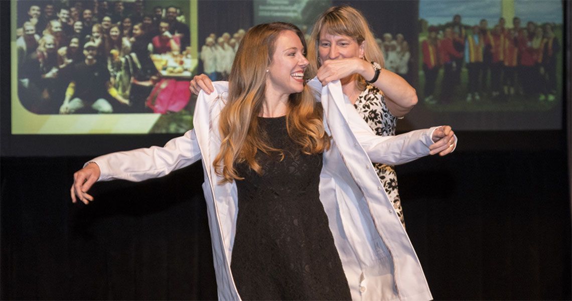 A GW PA student receives a white coat from a faculty member