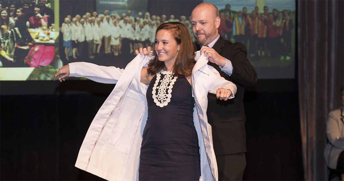 A GW medical student receives a white coat from a faculty member