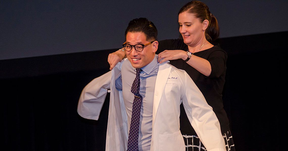 A Physician Assistant student receives a white coat from a faculty member