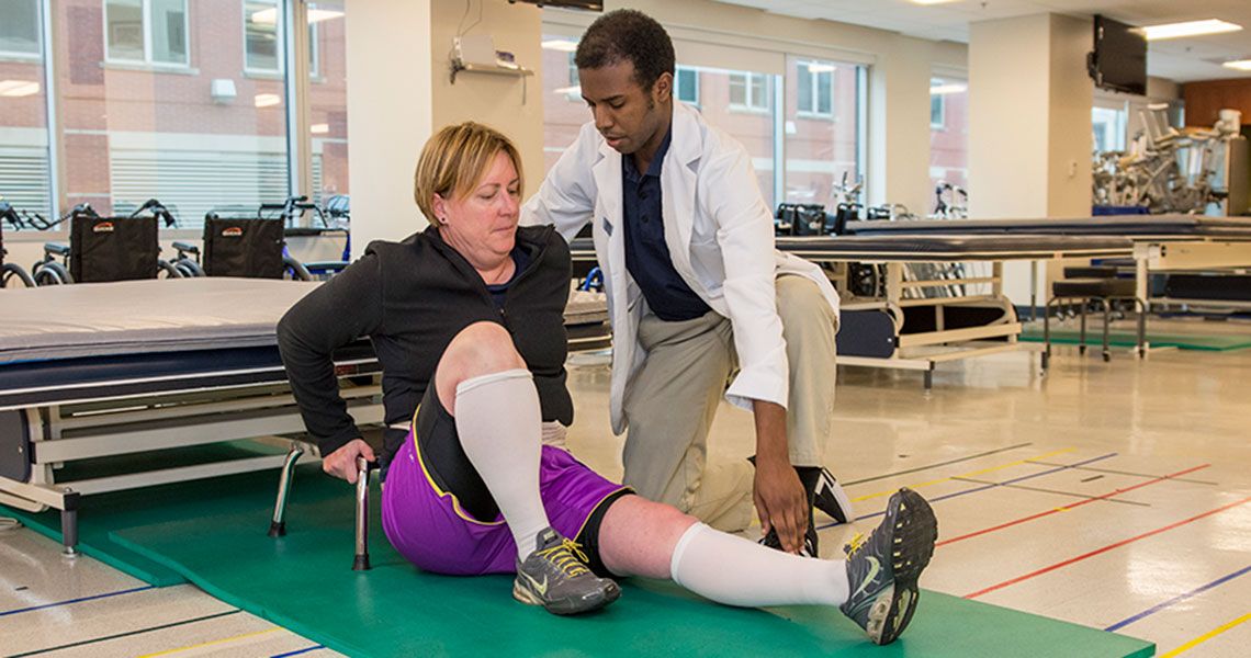 A physical therapist working with a patient stretching on a mat