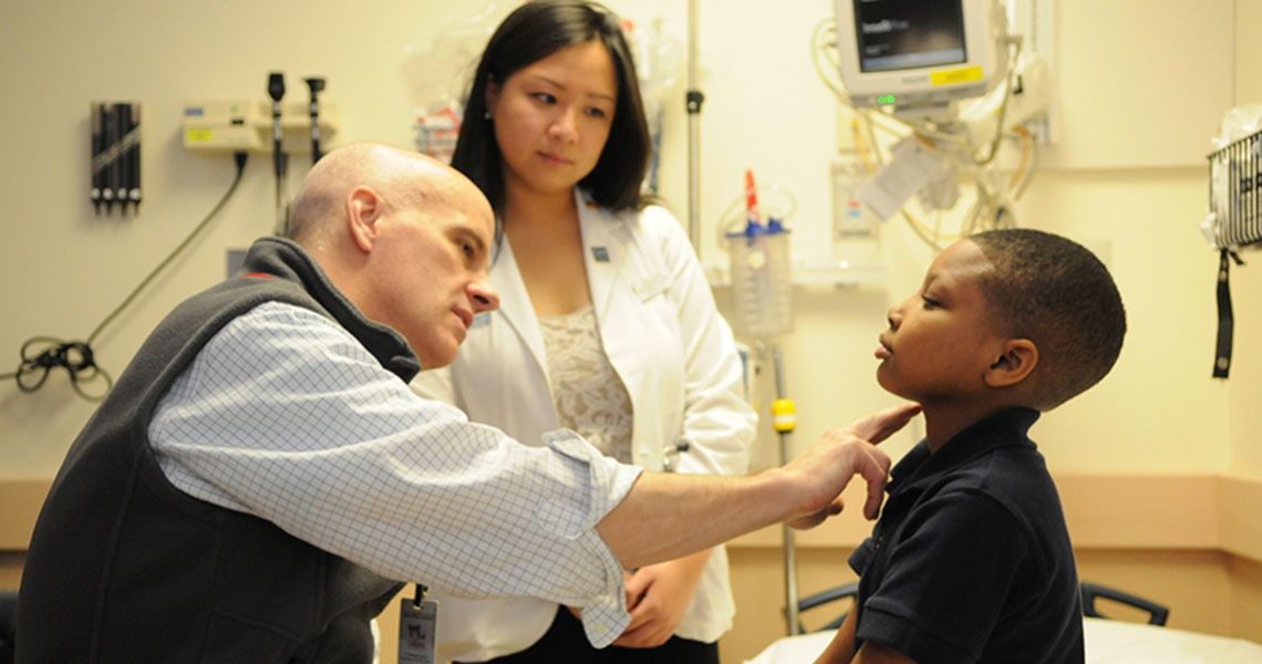 Dr. Stephen Teach and a nurse examining a child patient's neck 