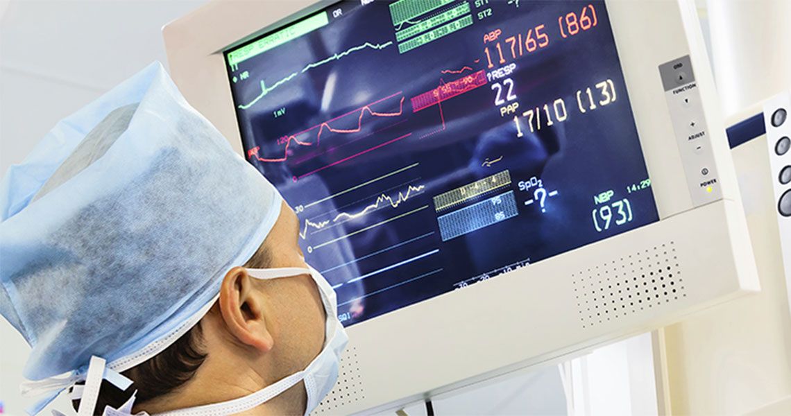 A medical professioal wearing a cap and mask looking at a display monitor