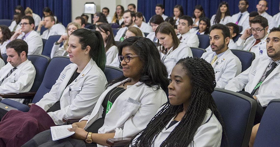 Students in white coats sitting in an auditorium