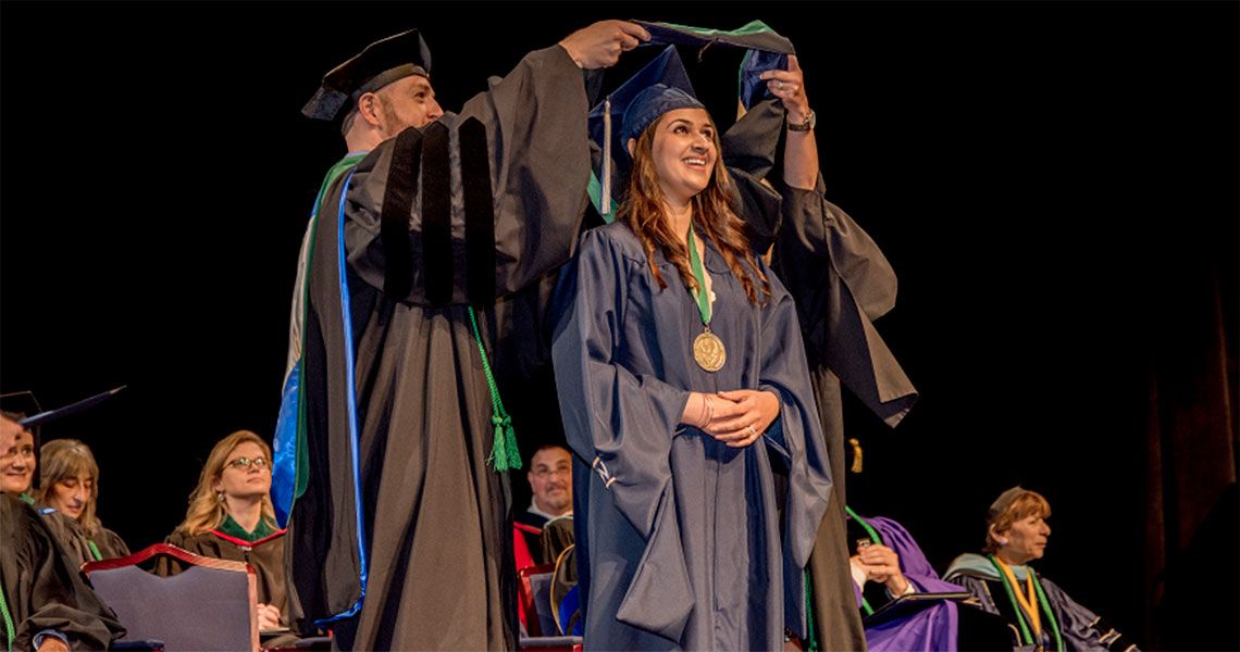 A graduate is hooded on stage at the GW Health Sciences graduation