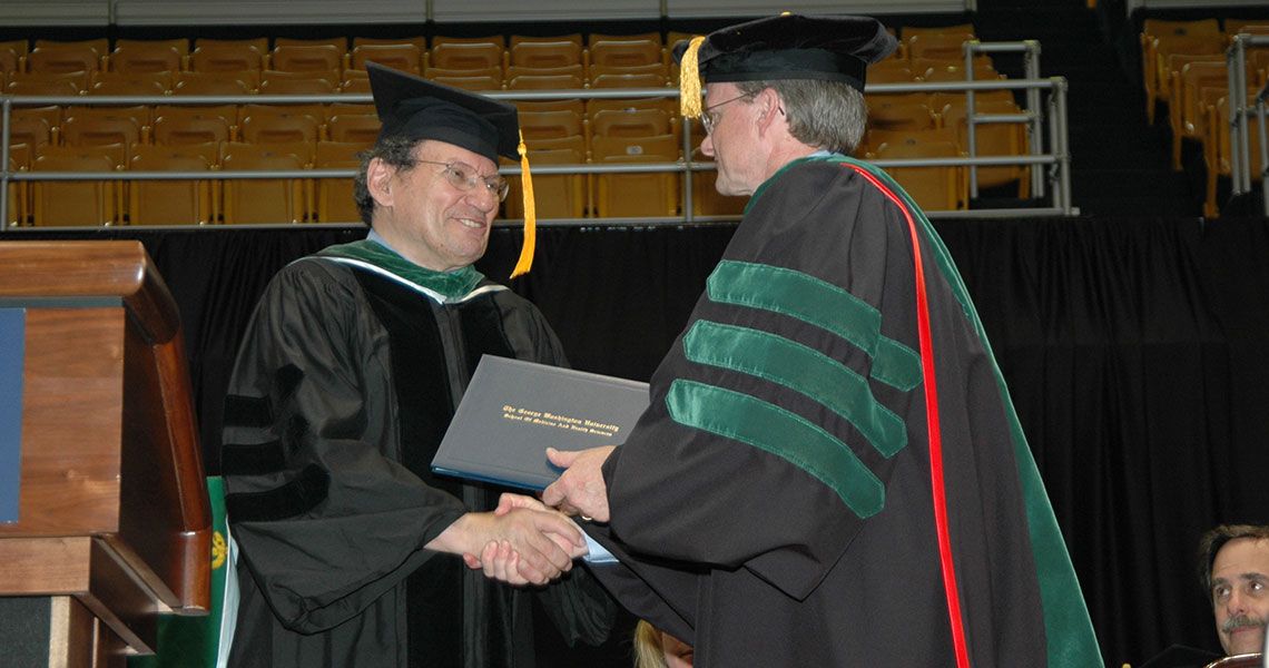 James Finkelstein in graduation regalia shaking hands with a SMHS faculty member