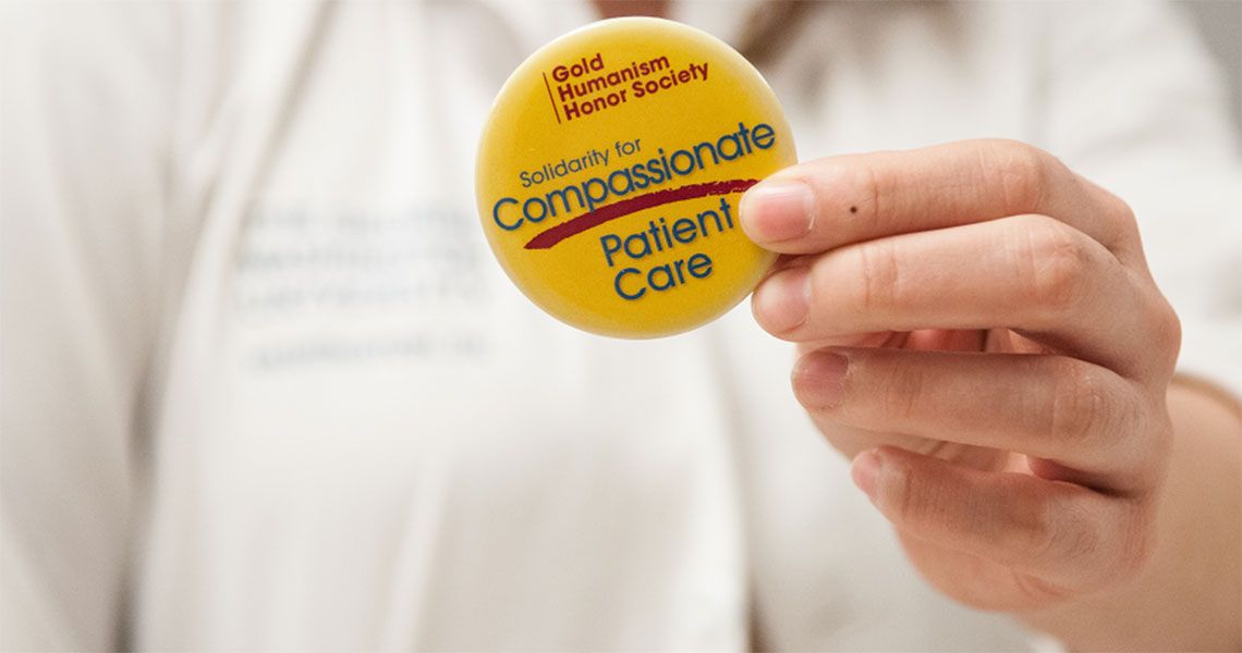 Person holding a golden pin with text on it | Gold Humanism Honor Society Solidarity for Compassionate Patient Care