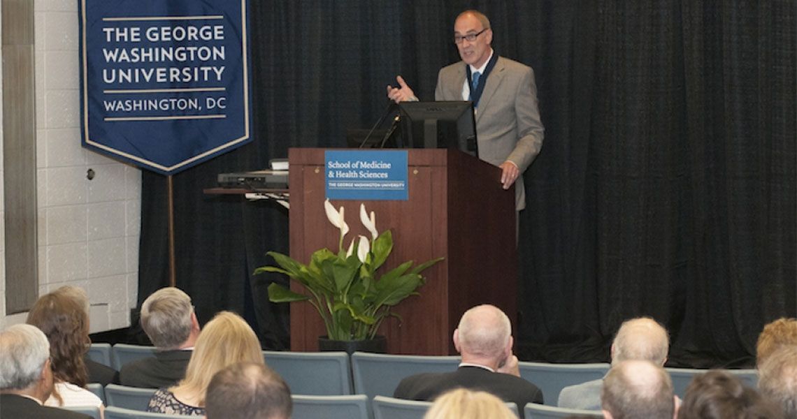 Dr. Robert Miller speaking from a podium to an audience