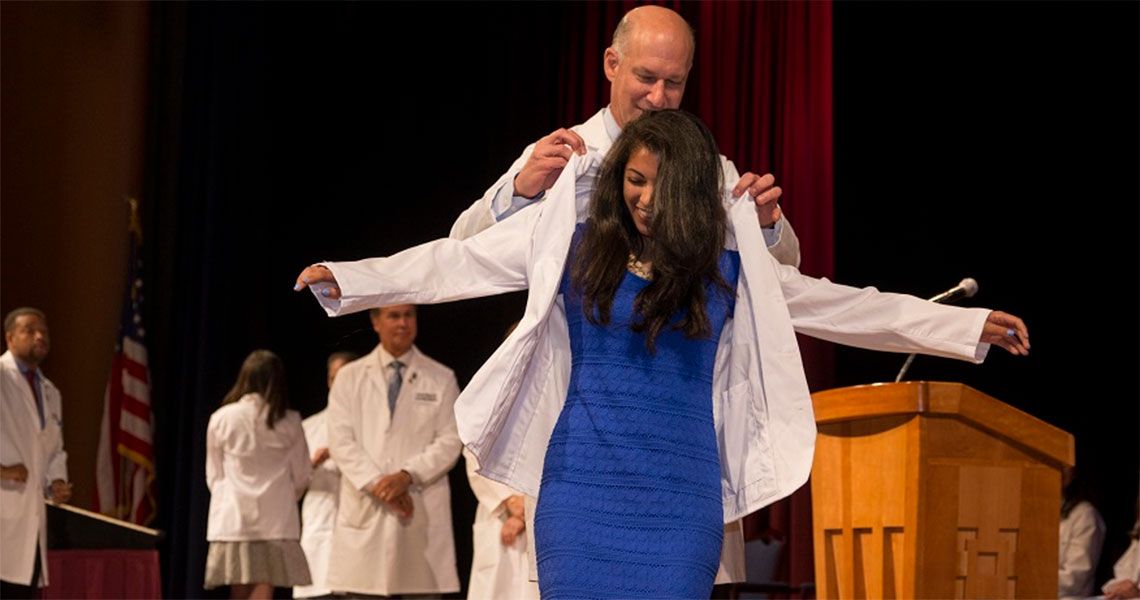 Dean Jeffrey Akman placing a white coat onto a student on stage