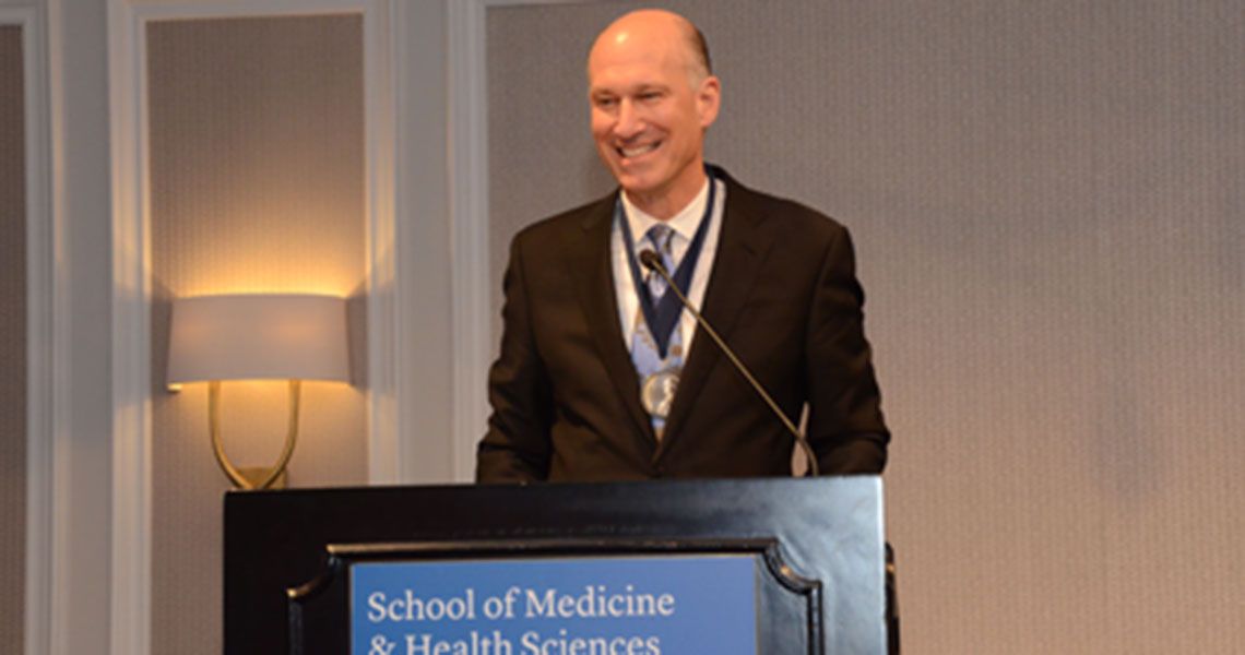 Dean Jeffrey Akman standing at a podium smiling