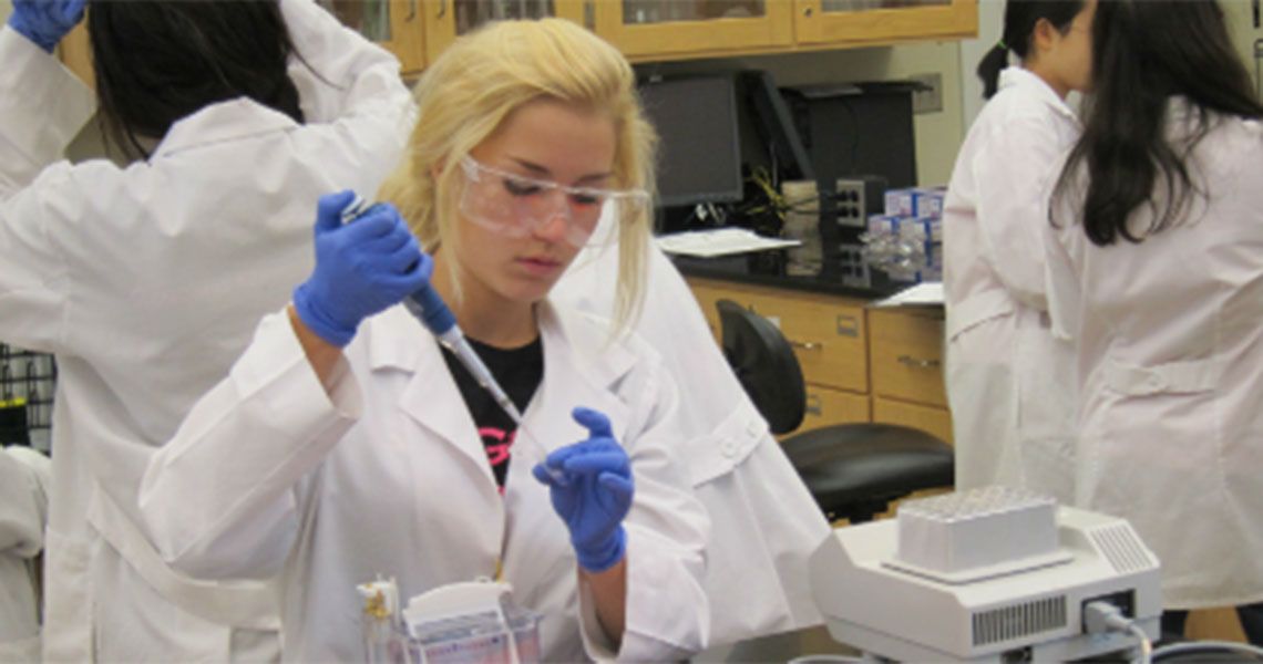 Woman in white lab coat and blue gloves using a pipette