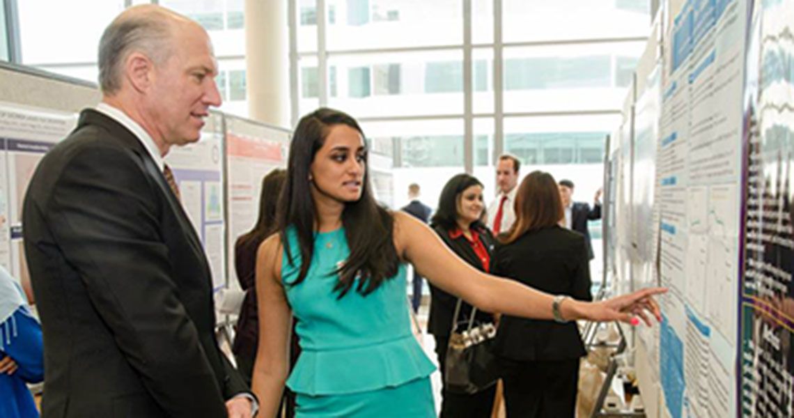 A medical student showing her research poster to SMHS Dean Jeffrey Akman