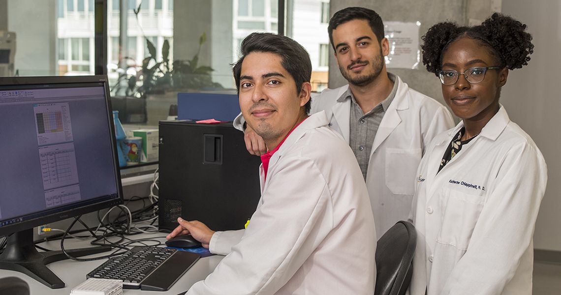 three people in lab coats smiling at the camera