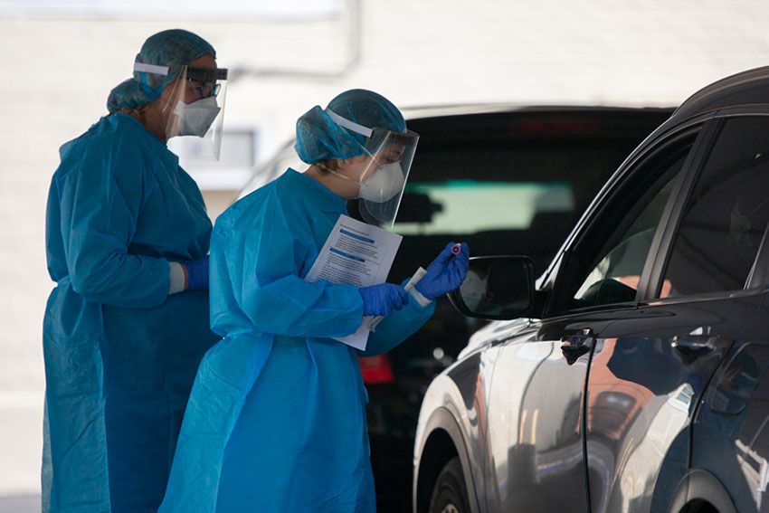 Two medical personnel in PPE collecting a person's covid-19 sample from their car