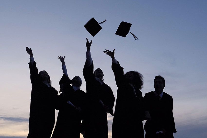 Silhouetted students toss graduation caps into the air