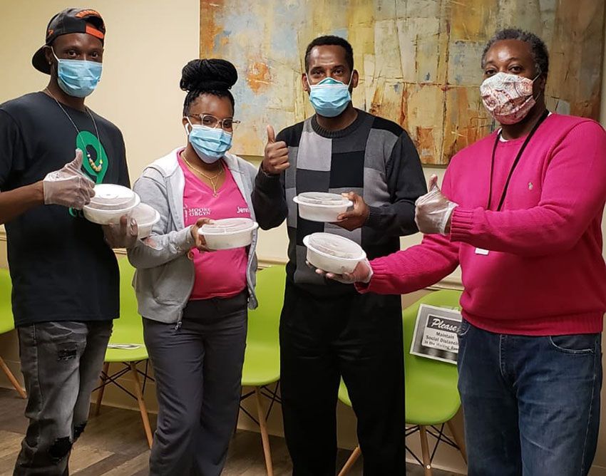 Masked Rodham Insitute staff hold meal containers and give thumbs-up