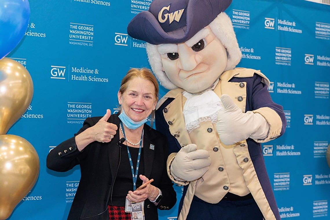 Dean Bass gives a thumbs up next to the GW Mascot