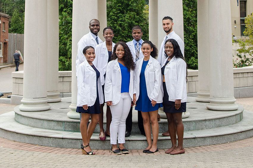 Eight GW medical students standing together in white coats in front of a rotunda