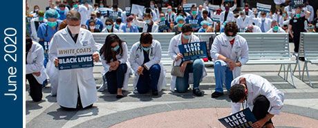 People in white medical coats kneeling in a public plaza holding signs | "June 2020"